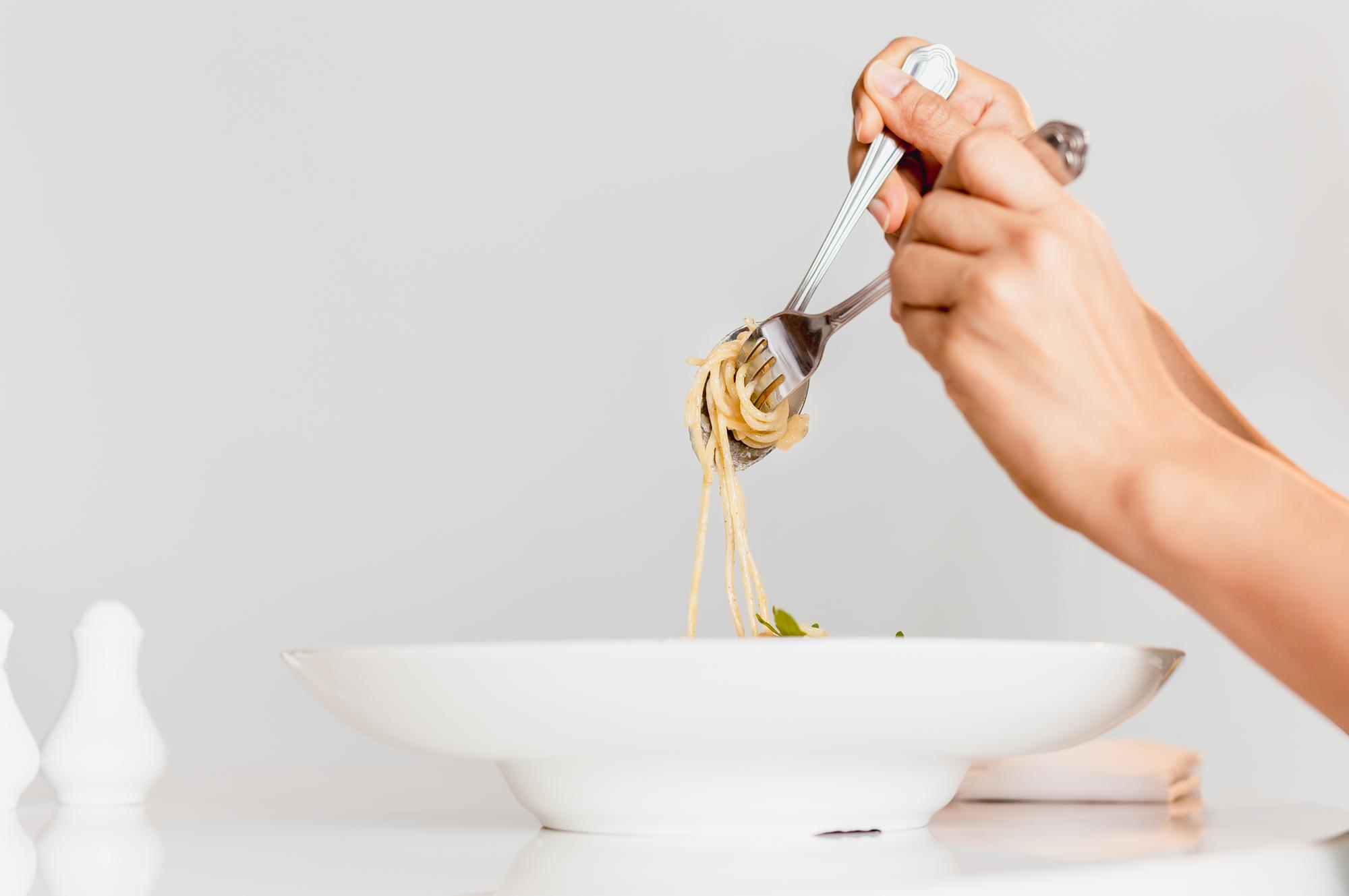 Mano che versa salsa su pasta